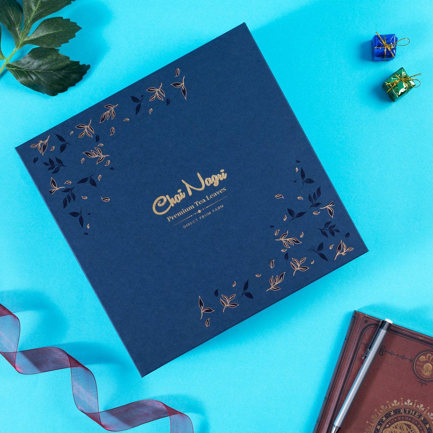 Geschlossene blaue Royal Teebox mit goldener Prägung, umgeben von Geschenkband und festlicher Dekoration.