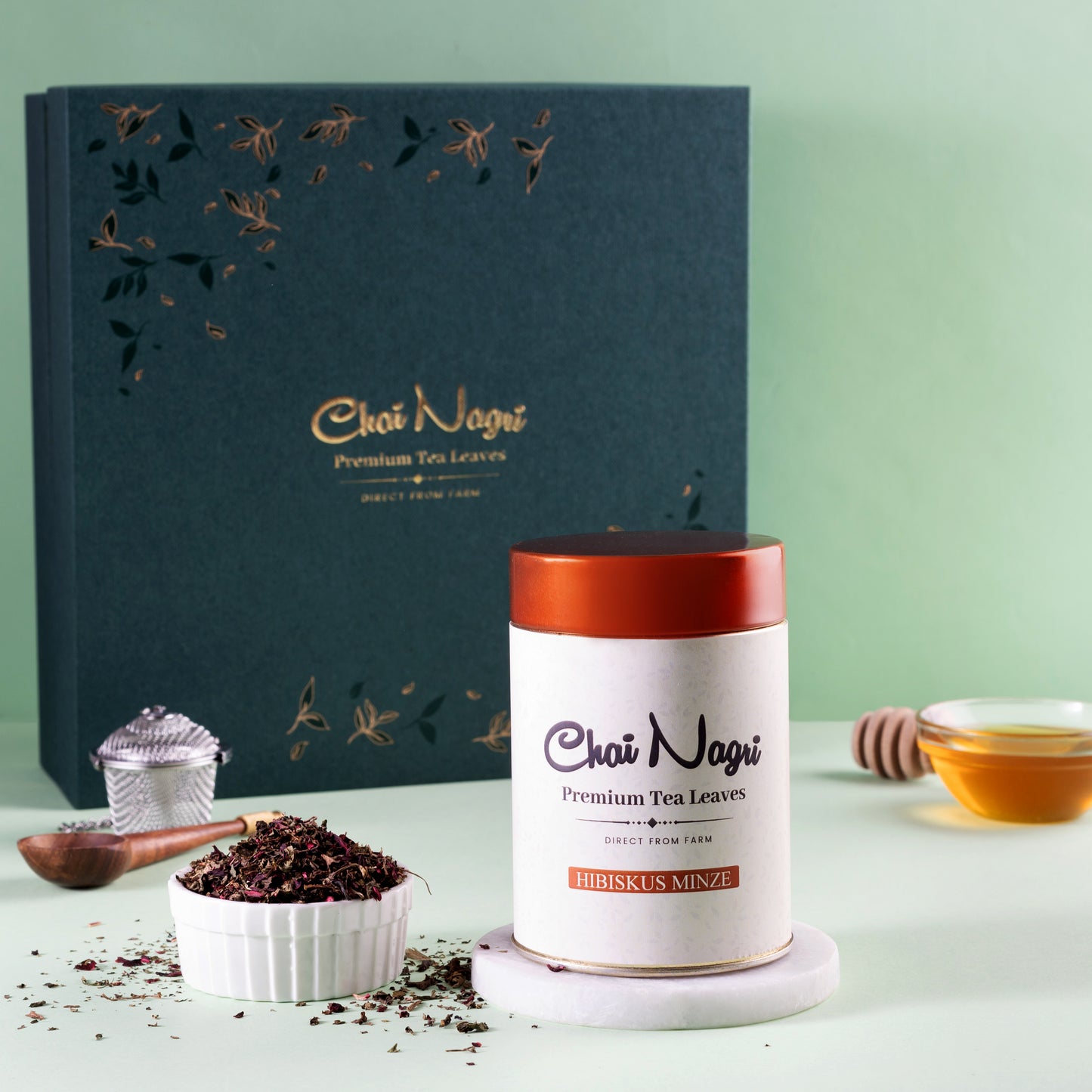 Hibiskus Minze Tee neben Royal Teebox, Holzlöffel, Honig und Teesieb – stilvoll inszeniert.