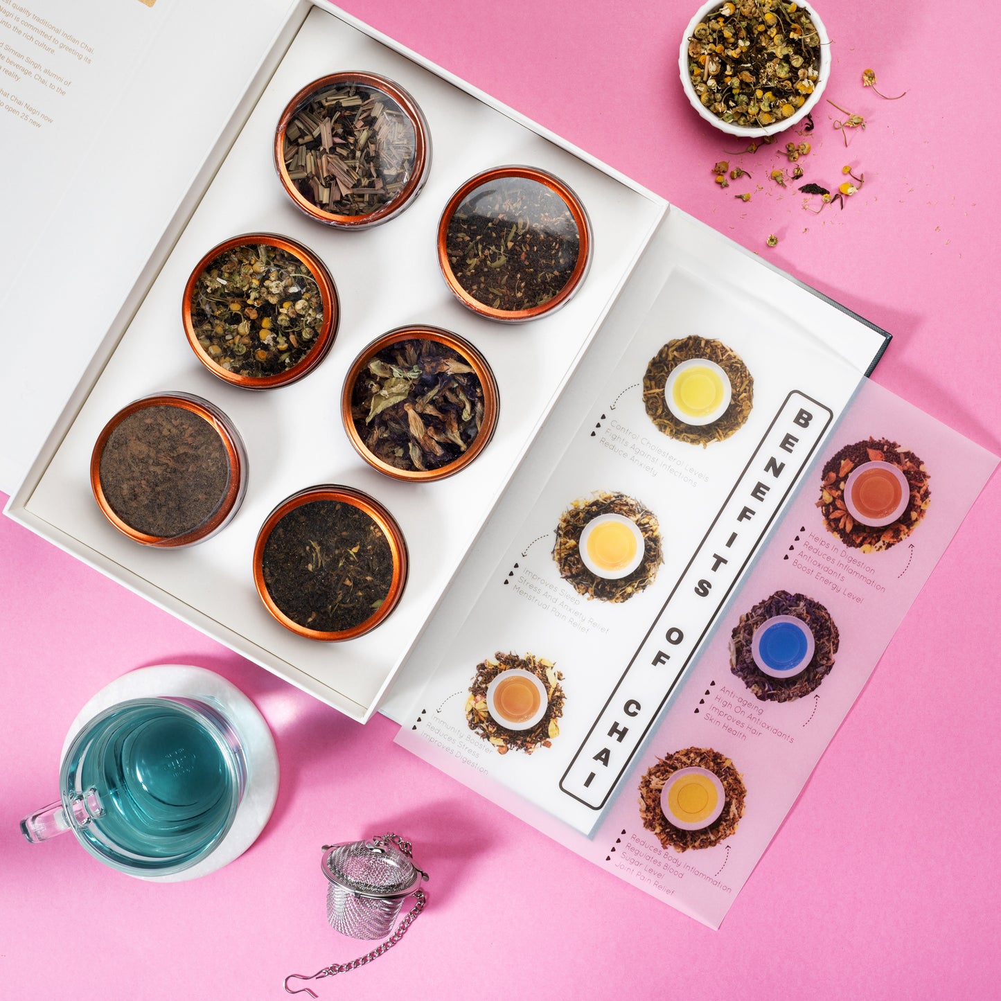 Offene Teebox mit 6 Sorten, Infoguide, Benefits of Chai und blauer Tee auf rosa Hintergrund.