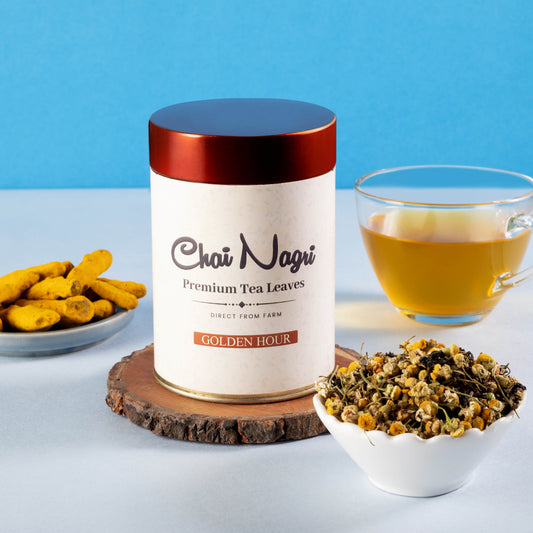 Golden Hour Teedose umgeben von losen Teeblättern, Kurkuma und aufgebrühtem Tee