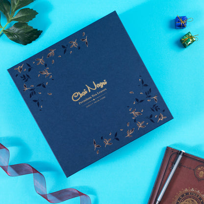 Geschlossene blaue Royal Teebox mit goldener Prägung, umgeben von Geschenkband und festlicher Dekoration.