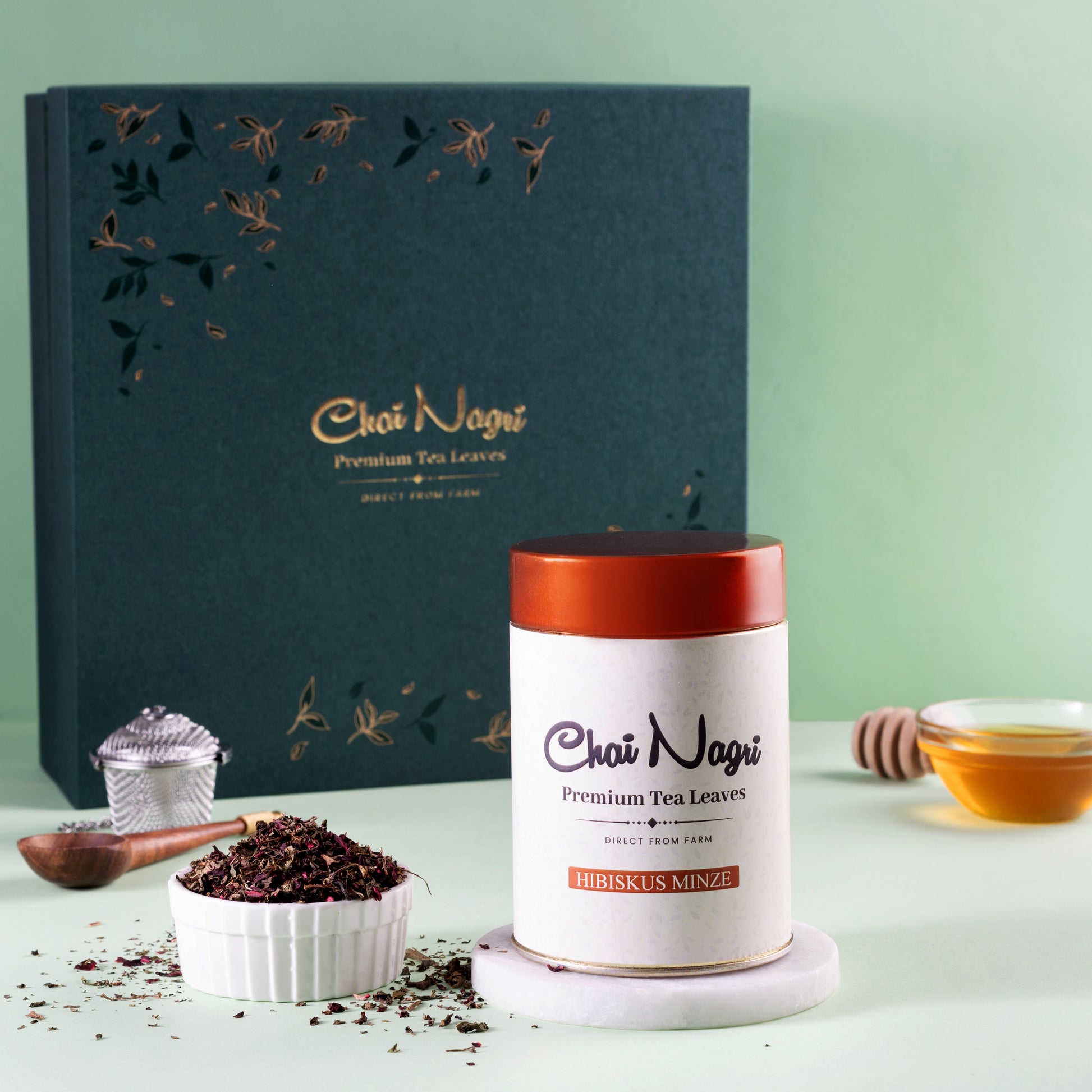 Hibiskus Minze Tee neben Royal Teebox, Holzlöffel, Honig und Teesieb – stilvoll inszeniert.